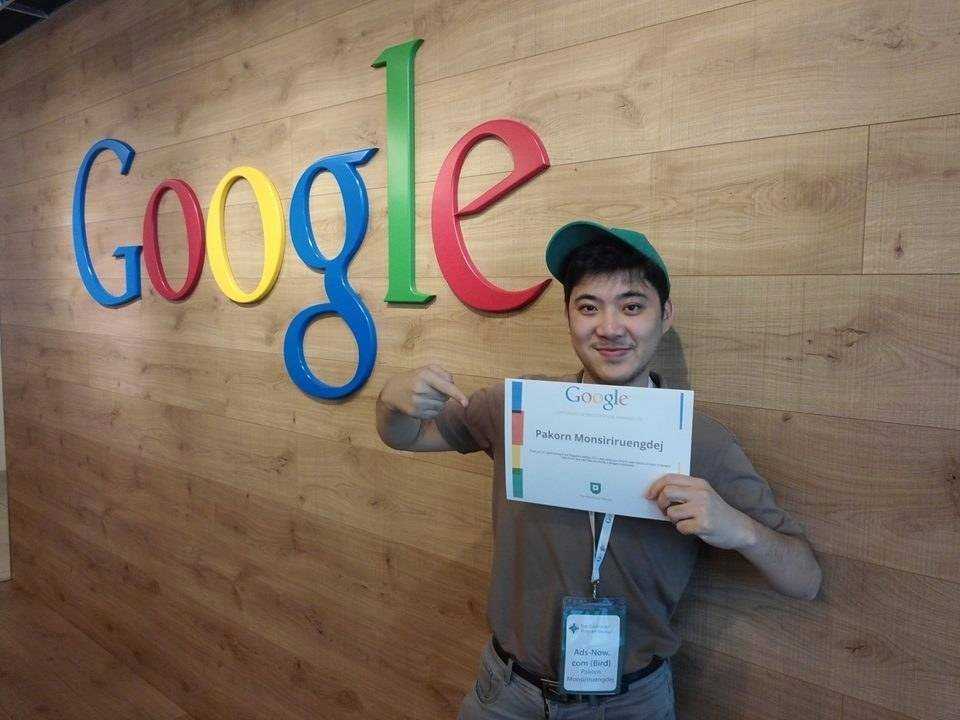 Pakorn holding a Google certificate at the Google office, smiling and standing in front of the colorful Google logo on a wooden wall.