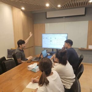 Meeting discussion at Pakorn office with team analyzing data on large monitor and laptops for business growth strategies.