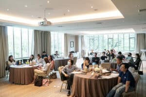 Professional corporate seminar room with attendees, presentation equipment, and large windows showing greenery, ideal for business meetings or conferences.